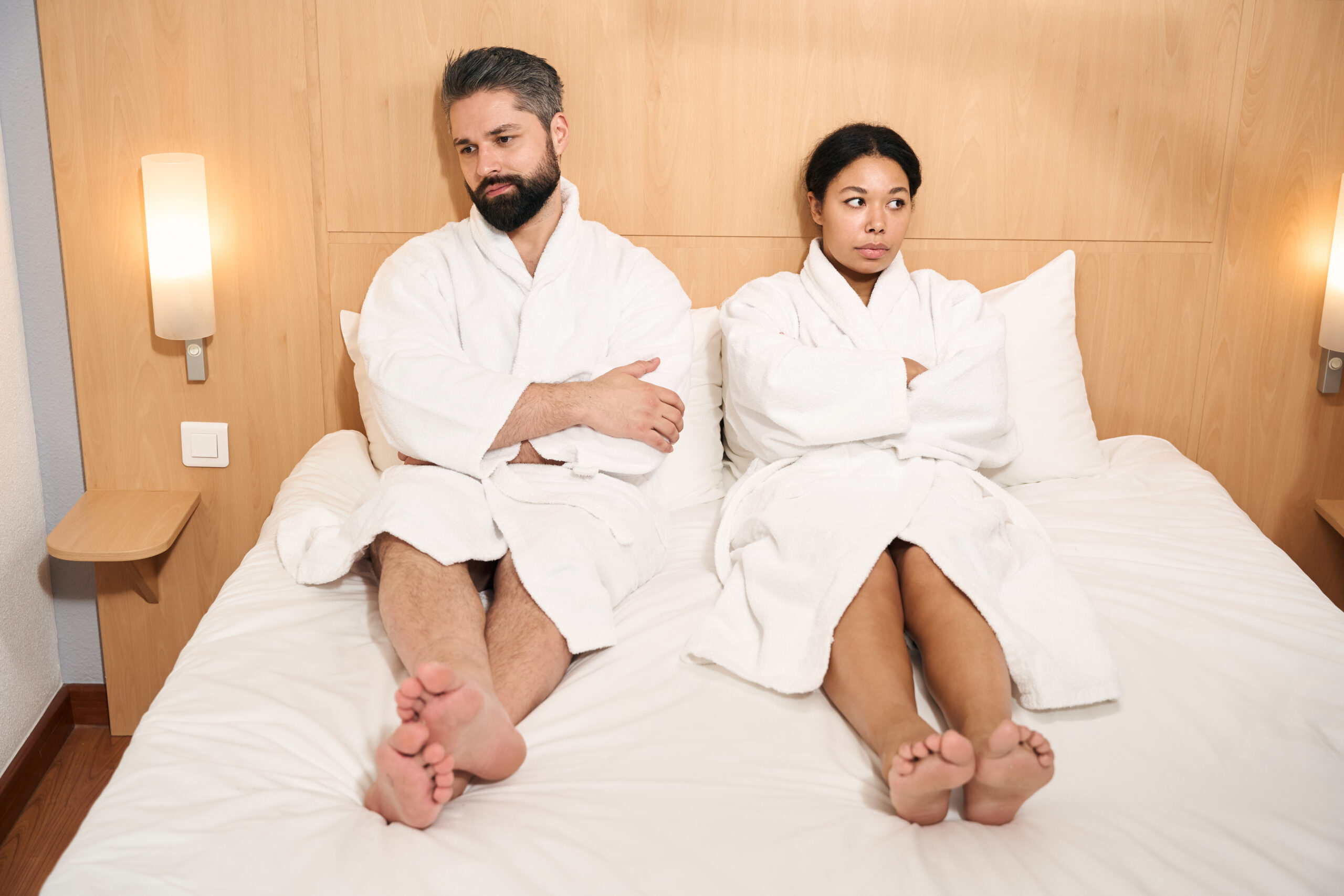 Low-spirited man and his despondent female companion seated in bed looking in different directions